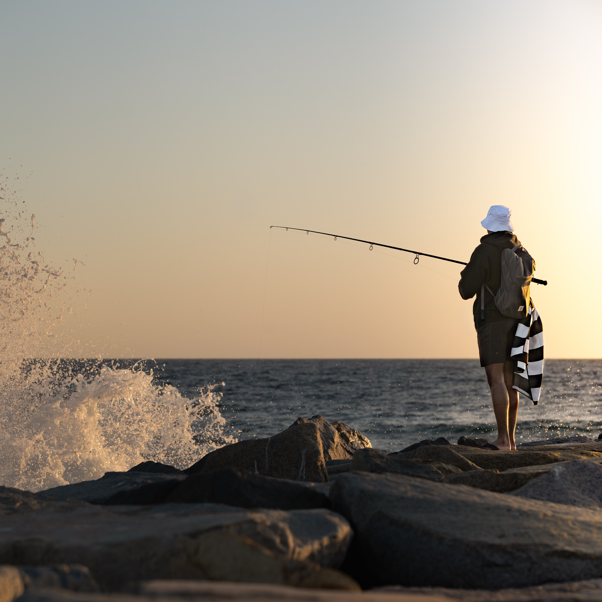Person fishing from rocks at golden hour